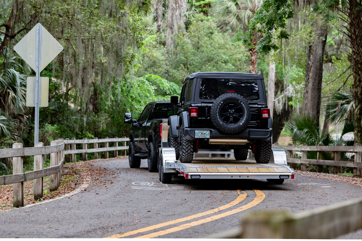 Black Jeep Loaded Onto Open Wood Deck Car Hauler On Paved Road